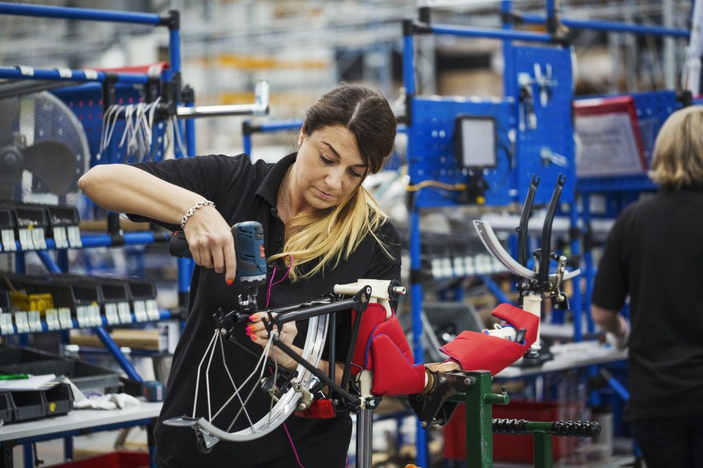 Female skilled factory worker assembling a bicycle in a factory working on the frame and wheels.