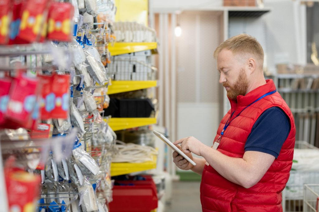 Young shop assistant in red uniform using tablet in hardware store